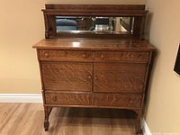 Front view of the oak buffet showing two small drawers, closed storage doors, matching wooden knobs, and mirrored back shelf.