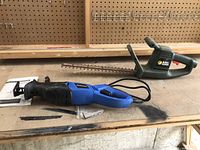 Mastercraft compact reciprocating saw and Black & Decker hedge trimmer on wooden workbench.