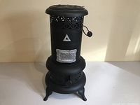 Front view of black metal vintage stove showing decorative cutouts, front door with latch, and handle on top