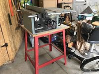 Photo showing Delta table saw mounted on a red metal stand in a garage setting.