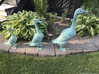 All three duck statues displayed on a garden border in front of plants