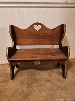 Front view of the wooden child's bench showing the heart-shaped cutout on the backrest and floral painted detail on the base.