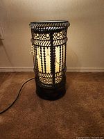 Front view of cylindrical lamp illuminated, showing metal frame and beads.