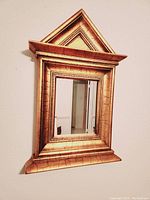 Front and angled side view of the gold framed mirror showing ornate textured gold frame and clear mirror glass
