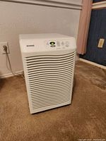 White Kenmore dehumidifier unit plugged in on carpeted floor, front-facing angle showing on LED display digital humidity reading.