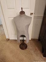 Front view of the fabric-covered mannequin torso on wooden stand in front of a white door, showing full height and structure.