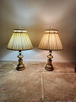 Pair of tall brass lamps with pleated fabric shades placed side by side on carpeted floor