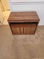 Front view of the wooden small storage table or TV stand showing flat top, open shelf, and closed double door cabinet below.