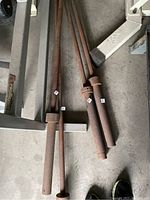 Four metal barbells laid on the floor, showing surface rust and discoloration. Two barbells have thicker cylindrical handles and threaded collars for weights; two are thinner and appear more worn.