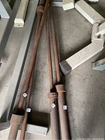 Photo shows one rusty metal barbell laying on a concrete floor among metal frame parts, with visible rust and wear.