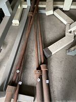 Three rusty barbells arranged on concrete floor near gym equipment base.