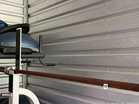 Barbell resting on white stand against a metal paneled wall, showing rust on the bar surface.