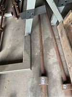 Photo of rusty metal barbell bar on concrete floor next to metal frame and wooden pallet.