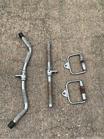 Four metal cable machine attachments laid out on concrete including EZ curl bar, straight bar, and two single-arm handles.