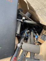Box containing metal frame parts, padded black bench seat, foam rollers, adjustment pins, and wiring for home gym bench press system.