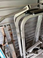 Photo showing white metal frame structure with curved bars and Exertec branding attached, some dirt and storage dust visible.