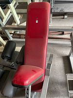 Incline bench with red padded backrest, seat and black foam roller leg support mounted on steel frame.