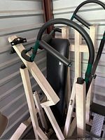 Disassembled exercise machine showing thick curved handles with foam padding and green grip accents attached to white metal frame components.
