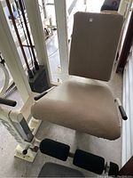 Full view of leg extension machine showing padded seat, backrest, and leg rollers in beige upholstery, white metal frame, weight stack visible at back.