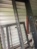 Large black metal uprights of squat rack leaning against wall, showing multiple adjustment holes and signs of wear.