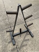 Black metal weight plate rack viewed from the front angle showing four angled cylindrical arms for holding plates and a central vertical post on base.