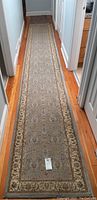 Full length angled photo of large runner carpet displaying overall size, design, and condition on wood floor