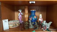 Shelf with assorted figurines including porcelain, brass, pottery vase, and beaded basket.
