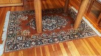 View of full width area rug under wooden dining chairs on hardwood floor showing pattern and border