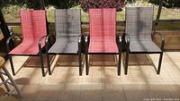 Set of four stacking patio chairs on tiled floor in sunlit enclosed patio, showing alternating red and grey mesh fabric seats and backs, black curved metal armrests and frames with some surface rust.
