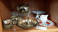 Full lot of porcelain tea set, fruit server, glass pie server and decorative plates on wooden shelf.