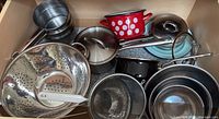 Drawer containing assorted pots, pans, enamelled pot, metal mixing bowls, perforated strainers and lids.