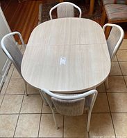 Overhead view of light wood finish oval dining table with four chairs around it, showing table surface with visible table leaf extension seam.