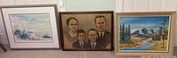 Three framed wall art pieces displayed against a white wall showing a landscape, family portrait, and a winter/coastal scene print.