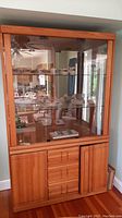 Front view of the Wambold dining hutch showing glass display area with dishes inside and wooden lower portion with drawers and doors.