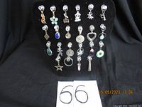 Full view of 22 assorted sterling silver vintage charms on black display stand, arranged in 5 rows showing shapes, colors, and worn patina