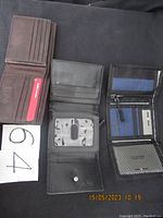 Three wallets opened laid flat on black fabric background showing card slots, ID windows, and compartments.