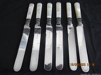 Photo of six cutting knives with polished blades, mother of pearl handles, and silver ferrules showing hallmarks.