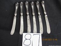Six table cutting utensils lined up with the handles at the top, showing metal blades and silver handles with ornate design.