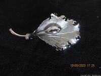 Front view of silver leaf-shaped brooch showing detailed veins and scalloped edges against a black background.
