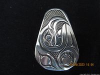 Front view of triangular carved silver First Nations Indigenous pendant showing detailed carved designs with textured background.
