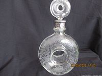 Full view of the etched round glass decanter with a central hole, showing the sterling silver collar on the neck and the glass stopper.