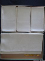 Boxed Irish damask tablecloth folded next to 12 matching napkins folded and arranged neatly inside the box.