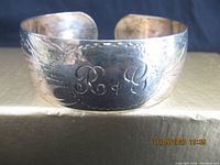 Front view of the sterling silver cuff bracelet showing engraved initials 'R + G' and floral pattern