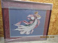 Full view of the framed needlepoint angel playing violin with corner protective bubble wrap, showing the entire artwork and frame.