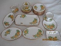 Full set layout showing all porcelain pieces including plates, cups, saucers, cream pitcher, and serving trays arranged on a white cloth.