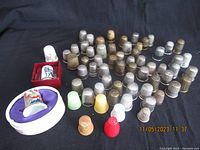 Full view of approx 60 assorted vintage and antique thimbles arranged on black cloth, including metal, porcelain and plastic types.