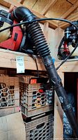 Red Homelite backpack leaf blower with flexible black intake hose on wooden shelf.