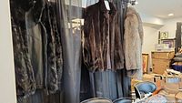 Three fur jackets hanging; two dark and one light shade visible.