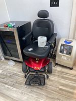 Front view of red Pride Jazzy Elite ES power scooter with black vinyl seat, joystick and footplate marked ‘Jazzy’.