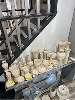 Wide view of numerous Lenox vases, candle holders, and bowls arranged on two-tier glass shelves under staircase.